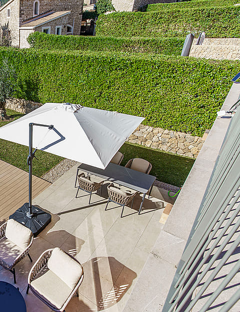 Aerial view of a private backyard featuring a swimming pool, sun loungers, dining area with a parasol, and stone walls.
