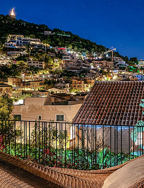 A stone-walled terrace at twilight, featuring a hammock, metal railing, and a view of hillside town lights in Genova.