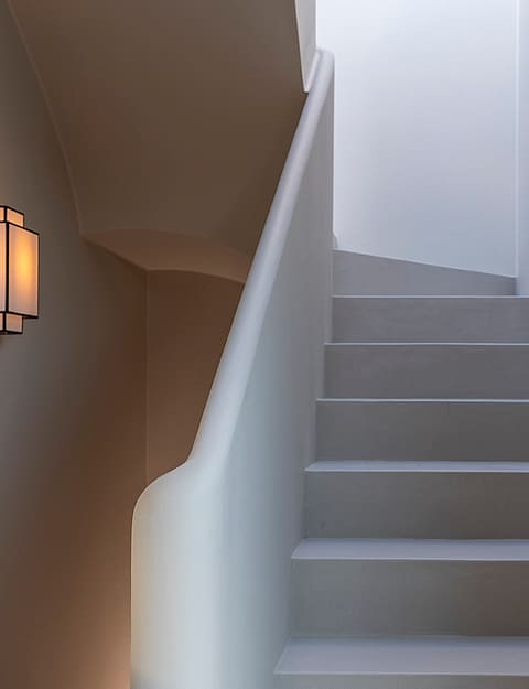 A minimalist microcement staircase with a curved balustrade, illuminated by a warm wall sconce and soft natural light.