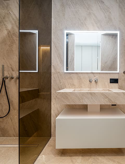 A modern bathroom featuring beige stone wall cladding, a floating vanity unit, a wall-mounted toilet, and a glass-enclosed shower.