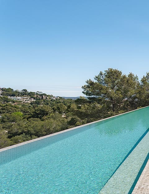 A long infinity lap pool runs alongside a minimalist concrete terrace with views of green Mediterranean hills.