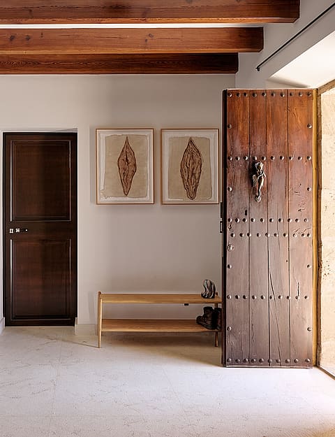 Entry foyer of a finca featuring white plastered walls, heavy dark wooden ceiling beams, and a large rustic timber door.