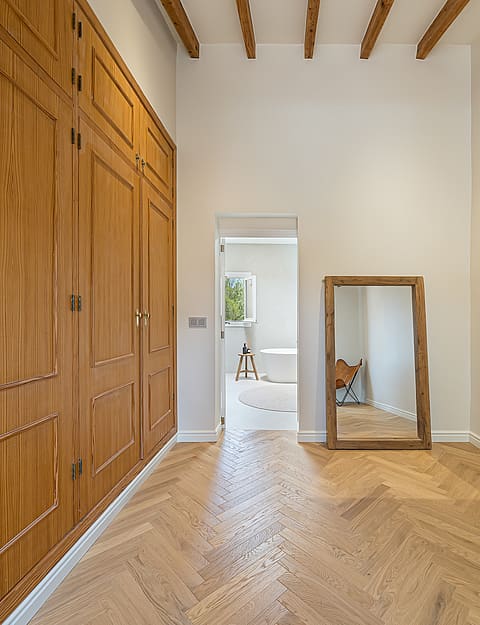 Dressing area with floor-to-ceiling wood wardrobes and herringbone parquet floors leading to an ensuite bathroom.