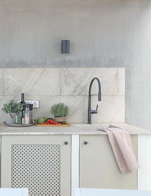 Outdoor kitchen featuring a stone backsplash, concrete wall, matte cabinetry, and a modern black faucet on a stone countertop.