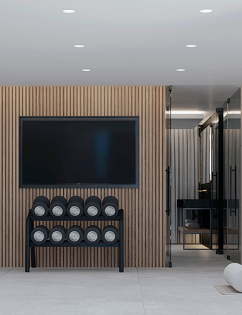 A modern home gym featuring vertical wood slat wall paneling, a rack of dumbbells, a cable pulley machine, and recessed ceiling lighting.