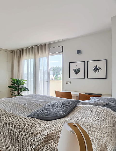 A modern bedroom with light wood flooring, a textured bedspread, and a large white built-in wardrobe with floor-to-ceiling doors.