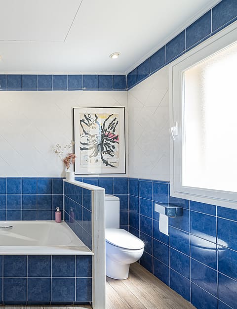 Bright bathroom featuring glossy blue and white wall tiles, a white vanity sink, a built-in bathtub, and a window.
