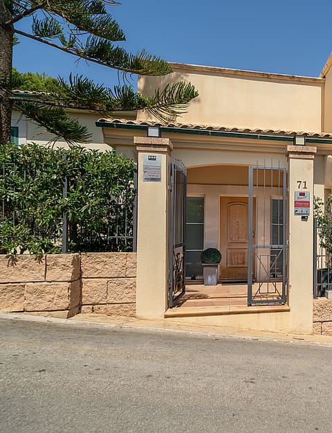 Exterior street-level view of a two-story villa featuring a pale rendered facade, green shutters, a private garage, and a gated entrance with stone accents.