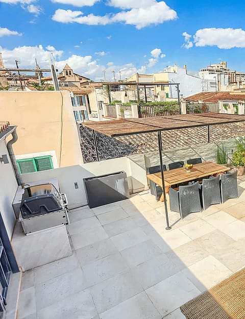 Aerial view of a paved rooftop terrace featuring outdoor dining furniture and seating area, overlooking the Old Town rooftops.
