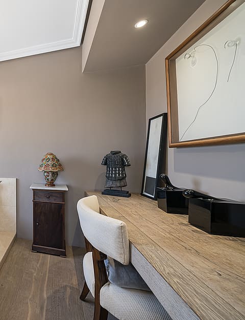 A bright bathroom with a built-in jetted white tub surrounded by beige stone, a stone-topped vanity, and a window with garden views.