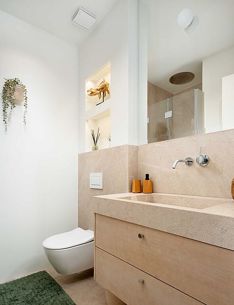 A modern guest bathroom featuring a wall-hung toilet, a vanity with natural stone surfaces, and recessed shelving.
