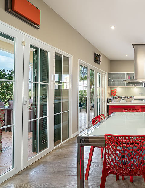 Modern kitchen with red cabinetry, a central dining table, and large glass doors leading to an outdoor terrace.