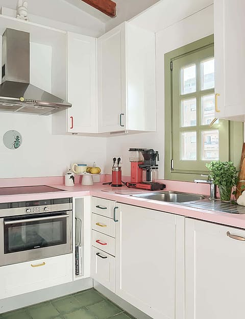 A small white galley kitchen with pale pink countertops, stainless steel appliances, and a green-framed window.