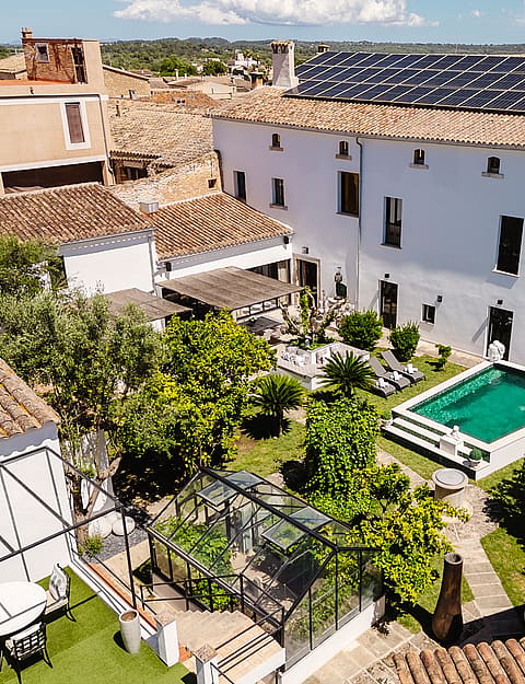 Aerial view of a Mediterranean townhouse central courtyard featuring a small swimming pool, surrounding gardens, and tiled roofs.