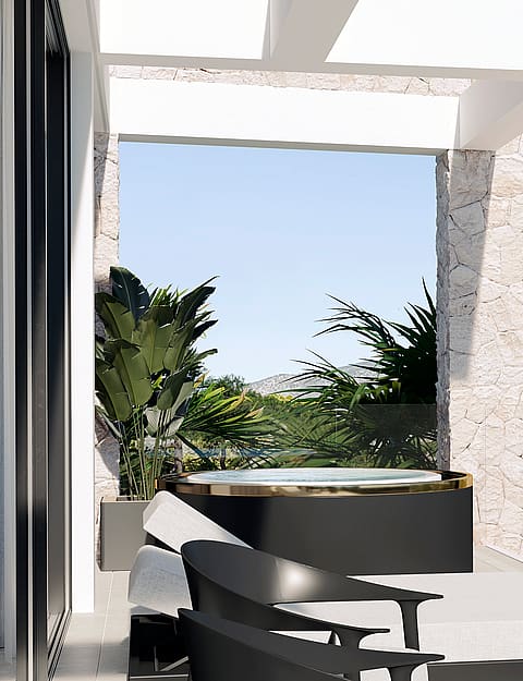 A covered terrace with a circular hot tub, black lounge chairs, stone walls, and green plants, opening to an outdoor view.
