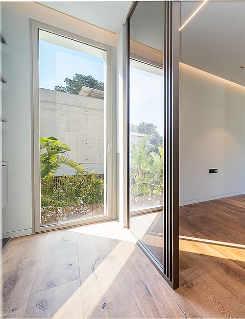 Empty modern room with wide oak floorboards, recessed linear lighting, and large sliding glass doors opening to greenery.