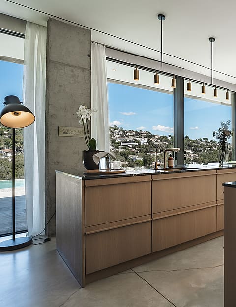 Contemporary kitchen featuring a wooden island with bar seating, dark countertops, and windows overlooking green hills.