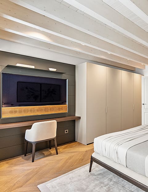 Contemporary bedroom featuring white exposed ceiling beams, chevron oak floors, built-in wardrobes, and an integrated desk.