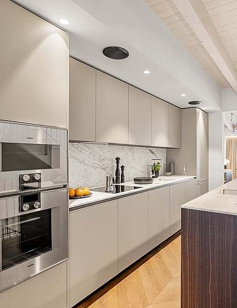 Modern kitchen featuring a dark wood island, marble countertops, white cabinetry, and herringbone oak flooring.
