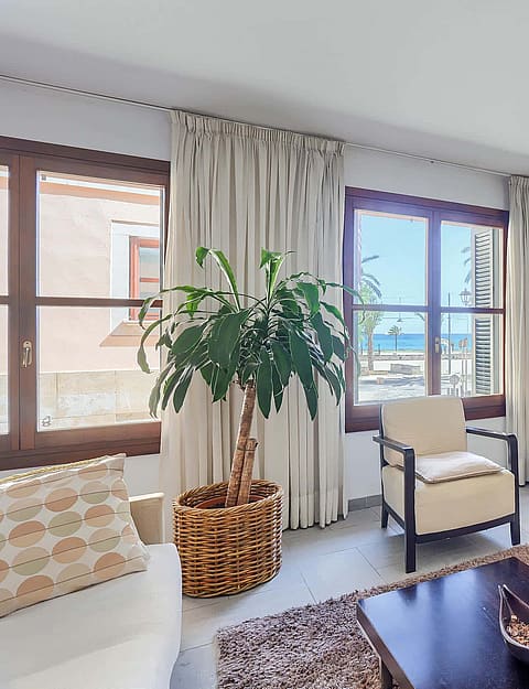 Living room with cream furniture, a wooden media console, potted plant, and windows framing a sea view in the Old Town.