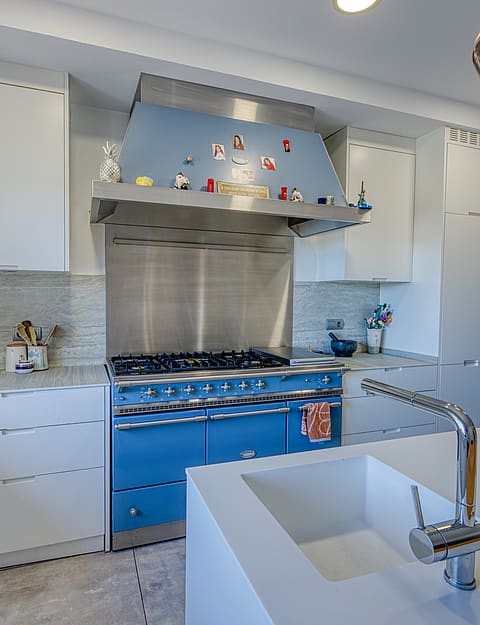 A modern kitchen featuring a bright blue range cooker, matching hood, white cabinetry, and a large central island with a sink.