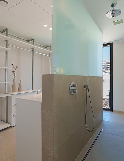 Baño moderno con ducha a ras de suelo, partición de cristal al ácido y zona de vestidor con estantes abiertos.