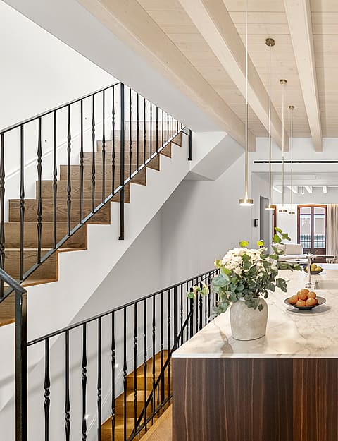 Kitchen island with marble counter and dark wood base beside a wooden staircase with black metal railings.
