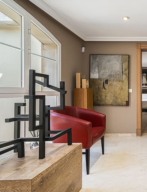 A bright mezzanine landing featuring a red leather armchair, a metal abstract sculpture, and framed wall art, overlooking the floor below.