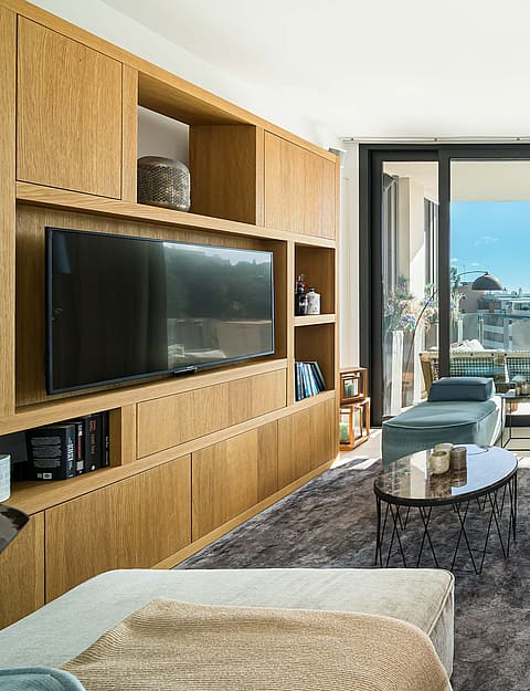 Modern living room featuring floor-to-ceiling oak cabinetry, neutral upholstered seating, and sliding glass doors to a terrace.