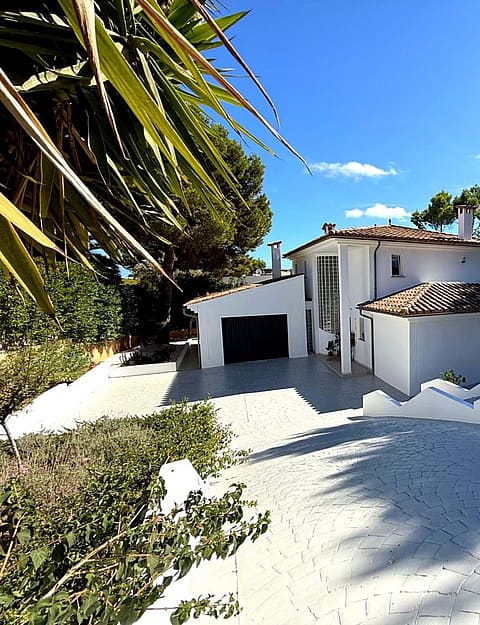 Front elevation of a white two-storey villa with terracotta roof, double garage and wide paved driveway