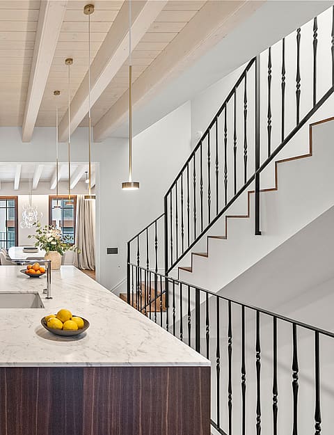 Kitchen island with marble top and dark wood base beside a staircase with black iron railings and exposed ceiling beams.