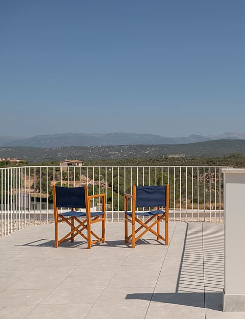 Elevated stone terrace with two wooden chairs facing a mountain landscape under a clear blue sky.