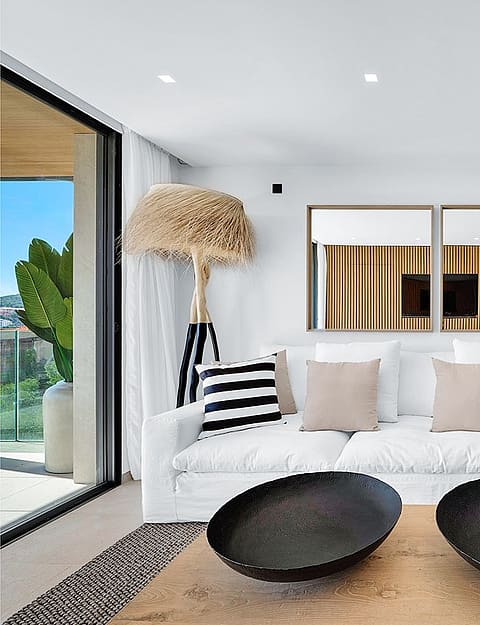 Modern living room featuring a white sofa with striped cushions, two black decorative bowls on a wooden coffee table, and vertical wood slat partitions.