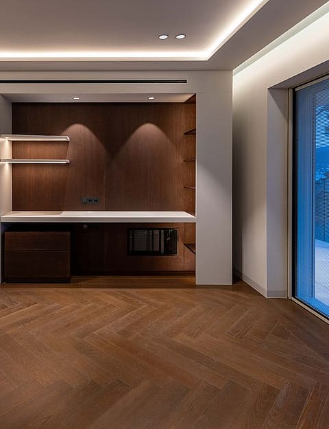 A modern home office space featuring dark wood herringbone flooring, integrated cabinetry with white countertops, and expansive glass sliding doors.