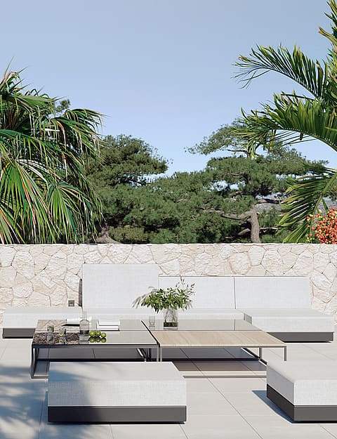 A contemporary outdoor terrace featuring low-profile modular white sofa seating and wooden coffee tables against a natural stone wall.