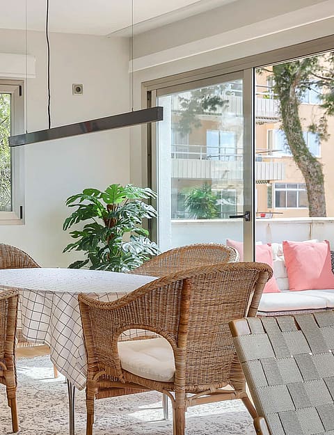 A dining space featuring four woven rattan chairs around a circular table, positioned near a window and a glass balcony door.
