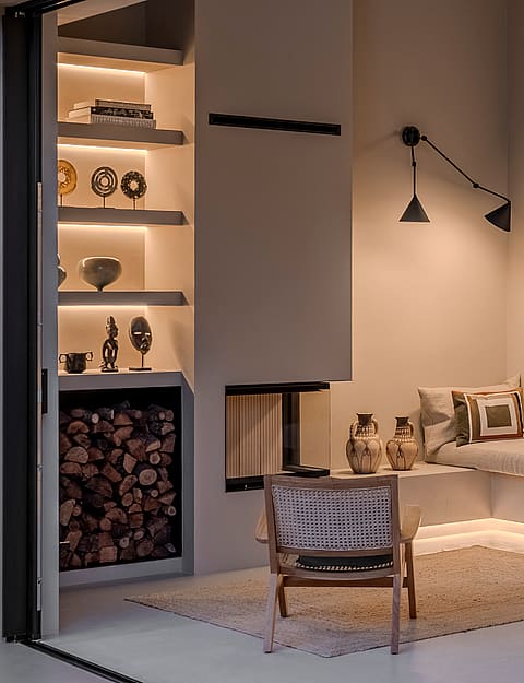 Interior view of a modern lounge featuring a glass fireplace, backlit shelving, and a floating banquette with LED lighting.