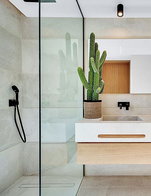Modern bathroom featuring a floating wooden vanity, double stone sinks, black matte fixtures, and a glass-enclosed shower.