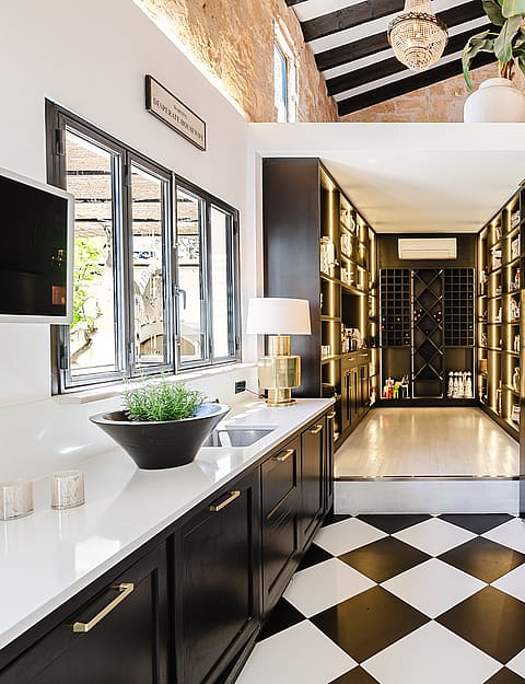 A modern kitchen with black cabinetry, white countertops, and a black-and-white checkered floor leading into a back pantry.