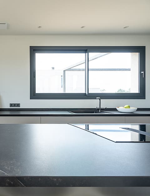 Contemporary kitchen featuring matte grey cabinets, dark stone countertops, wooden shelving unit, and integrated appliances.