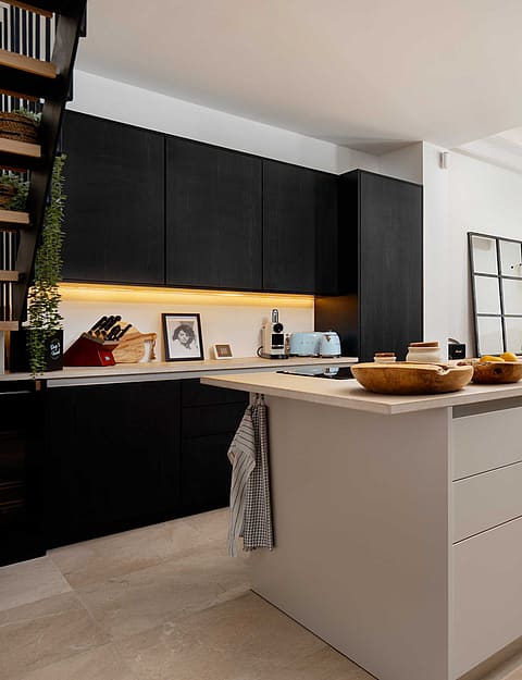 Open kitchen with black cabinetry, a pale stone-topped island, and a dining table and French doors visible beyond.