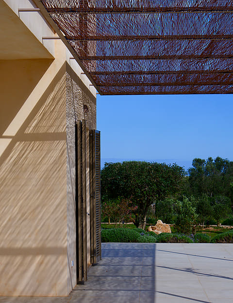 A modern outdoor terrace in Santanyí featuring a geometric laser-cut metal pergola casting intricate shadows on stone walls.