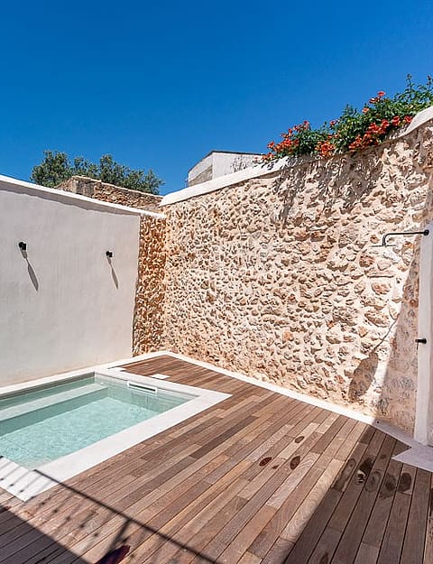 A small rectangular plunge pool set into a wooden deck inside a private courtyard with high white and stone walls.