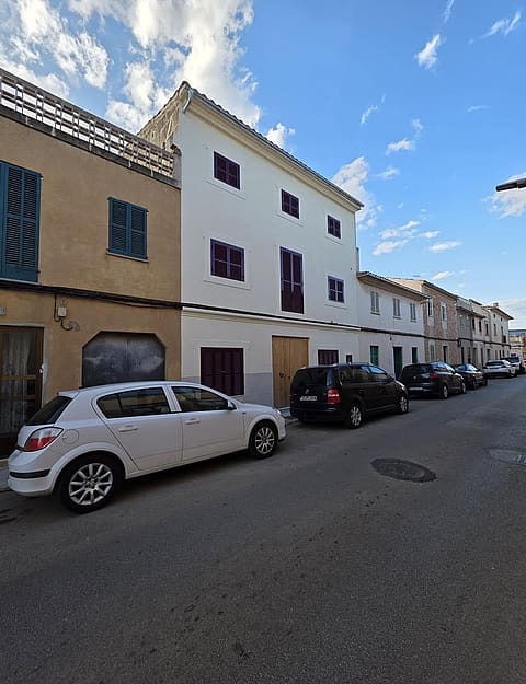 Exterior view of a multi-story townhouse in Campos featuring a white rendered facade, wooden shutters, and street parking.