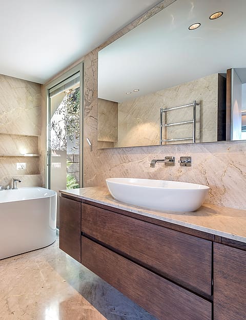 Contemporary bathroom featuring a dark wood vanity, white vessel sink, and large wall-to-wall mirror with travertine tile walls.