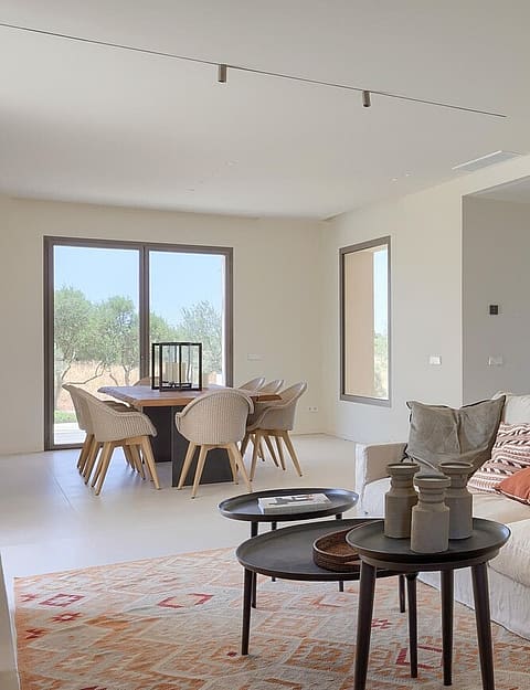 An open-concept living and dining space with a cream fabric sofa, nested coffee tables, and a wooden dining set near a large window.
