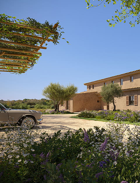 Exterior view of a traditional stone finca with natural terracotta walls, wooden shutters, and a gravel driveway.