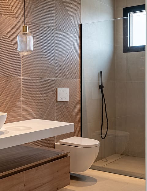 Modern bathroom interior with white vessel sink on a floating vanity, a circular wall mirror, and a geometric-textured accent wall.