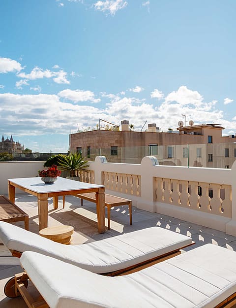 A sunny rooftop terrace in Santa Catalina with white sun loungers, a wooden dining table, and a decorative stone balustrade.