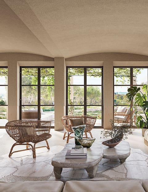 Spacious living room featuring arched textured ceilings, large glass-paned doors, a curved beige sofa, and natural stone flooring.